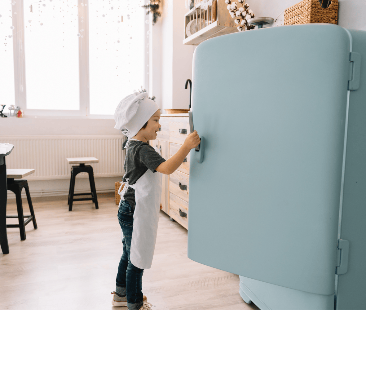 Little boy with a chef hat and apron on opening fridge door with no custom magnets on it